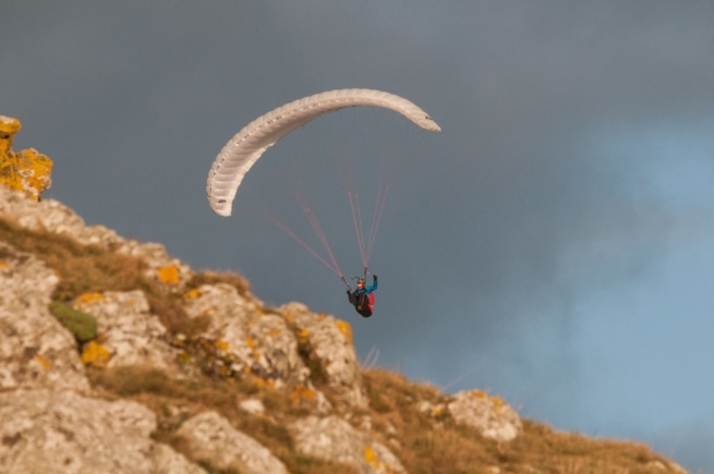 A paraglider soaring high above the cliff top at L'Etacq, St. Ouen, Jersey, Channel Islands