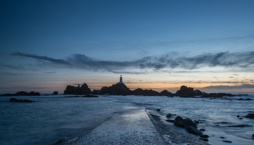 Corbiere Lighthouse after sunset as the tide recedes over the causeway, St. Brelade, Jersey, Channel Islands