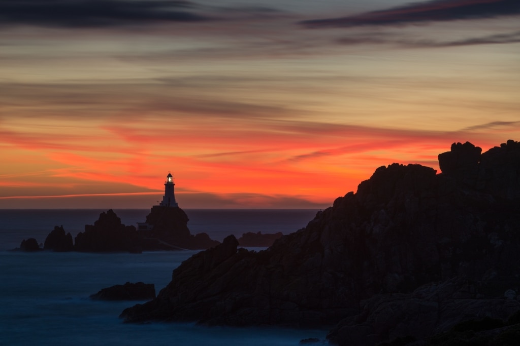 Corbiere Lighthouse and silhouetted cliffs with vibrant clouds after sunset from La Rosiere, St. Brelade, Jersey, Channel Islands