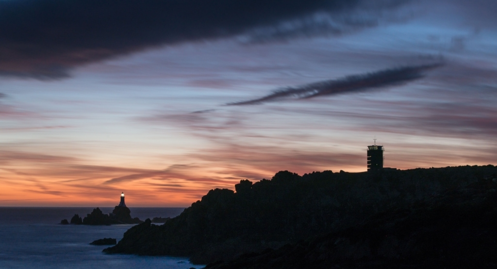 Corbiere Lighthouse and silhouetted cliffs and the Radio Tower with vibrant clouds after sunset from La Rosière, St. Brelade, Jersey, Channel Islands