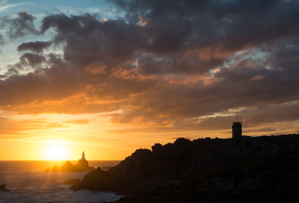 Corbiere Lighthouse and silhouetted cliffs and the Radio Tower with vibrant clouds at sunset from La Rosière, St. Brelade, Jersey, Channel Islands