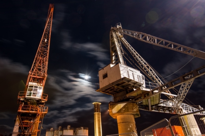 Cranes on Victoria Pier at night with the moon between them poking through the clouds, and The Power Station behind, St. Helier Harbour, St. Helier, Jersey, Channel Islands