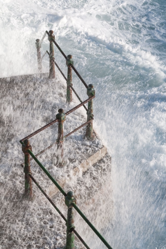 High tide splashing over the railings on the sea front at L'Ouziere Slip, St. Ouen's Bay, St. Peter, Jersey, Channel Islands at high tide with strong winds, rough sea and big waves