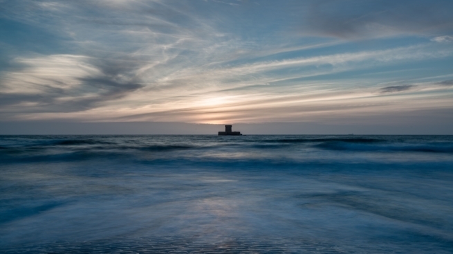 Long exposure seascape showing La Rocco Tower at sunset and the waves on Le Braye Slipway at high tide, St. Brelade, Jersey, Channel Islands