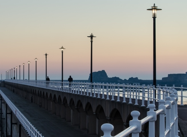 Lamps and railings at St. Helier Marina at sunset with St. Helier Hermitage in the background, St. Helier, Jersey, Channel Islands