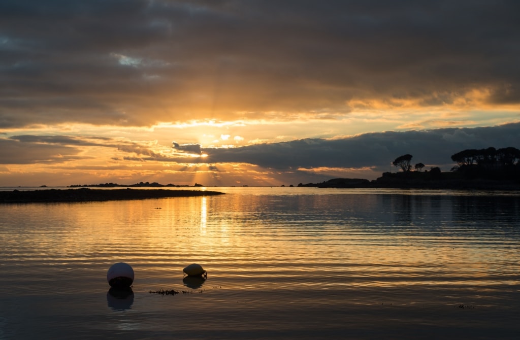 Orange sun bursting through the clouds and shining on the sea at sunset at Le Hocq, St. Clement, Jersey, Channel Islands