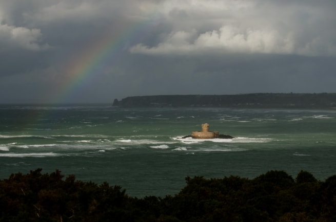 Wild and windy seascape after heavy rain showing a rainbow and La Rocco Tower and the whole of St. Ouen's Bay from high above on the headland at L'Oeillere, St. Brelade, Jersey, Channel Islands