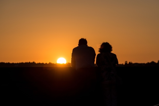 Romantic moment as a couple watch an orange sunset together at The Iron Tree, St. Helier Marina, St. Helier, Jersey, Channel Islands