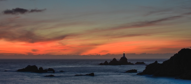 Silhouette of Corbiere Lighthouse and cliffs with vibrant clouds at sunset from La Rosiere, St. Brelade, Jersey, Channel Islands