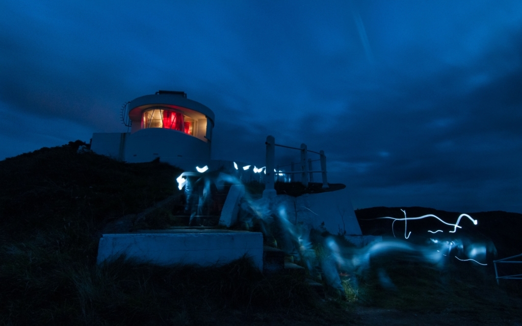 Sorel Point Lighthouse at night as three fishermen climb back up the cliff path with their torches on, St. John, Jersey, Channel Islands