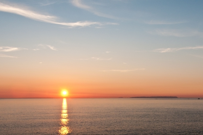 Sunset on the sea from the cliff path at Devil's Hole, St. Mary, Jersey, Channel Islands with Sark, Herm and Guernsey visible