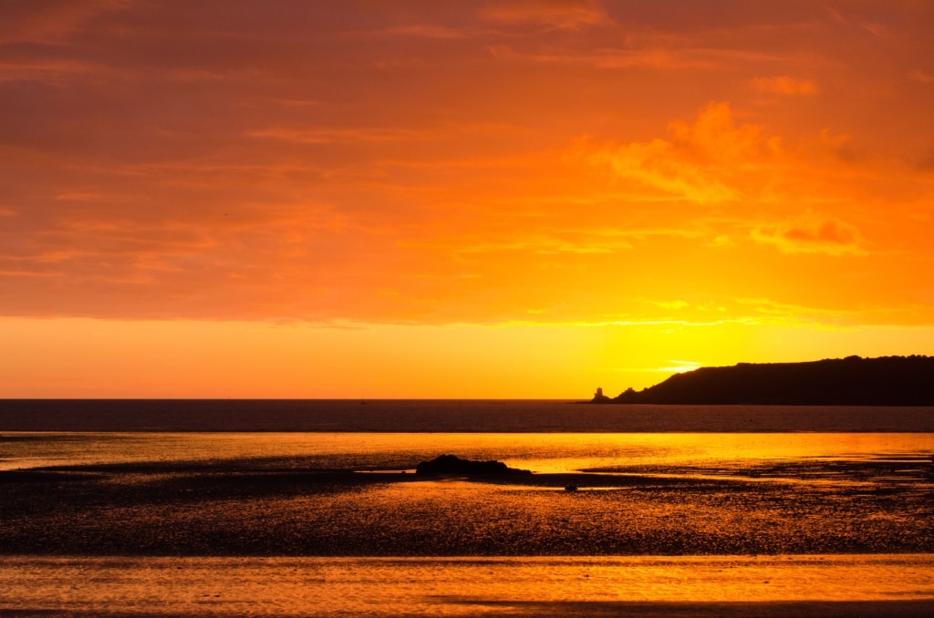 Glorious orange sunset reflected in the sand looking accross St. Aubin's Bay towards Noirmont Headland, West Park, St. Helier, Jersey, Channel Islands