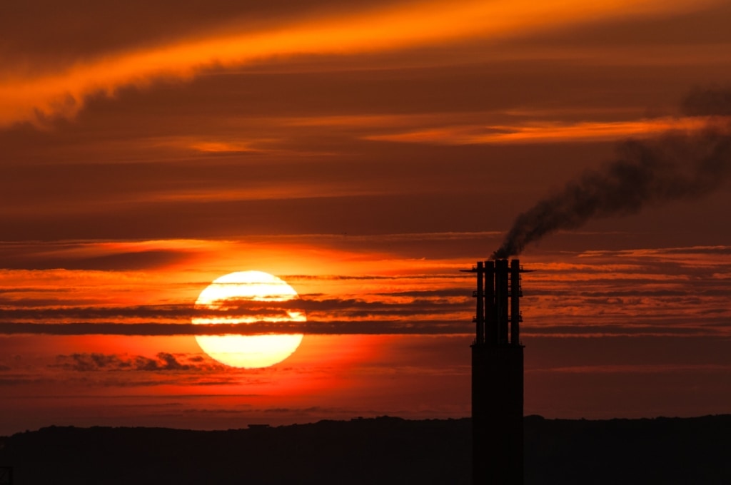 Large sun on a long zoom at sunset with a silhouette of La Collette Power Station next to it, plus smoke pollution and interesting cloud patterns, taken from a field off Les Huriaux, Grouville, Jersey, Channel Islands