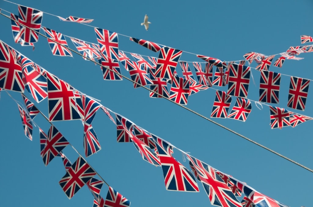 British Union Jack bunting in front of the parish hall at St. Ouen, with a blue sky behind and a seagull soaring high above, Jersey, Channel Islands